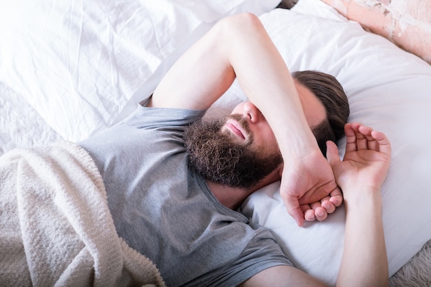 Lundi matin encore. Paresse. Homme couché dans son lit couvrant les yeux avec le bras contre la lumière du jour.