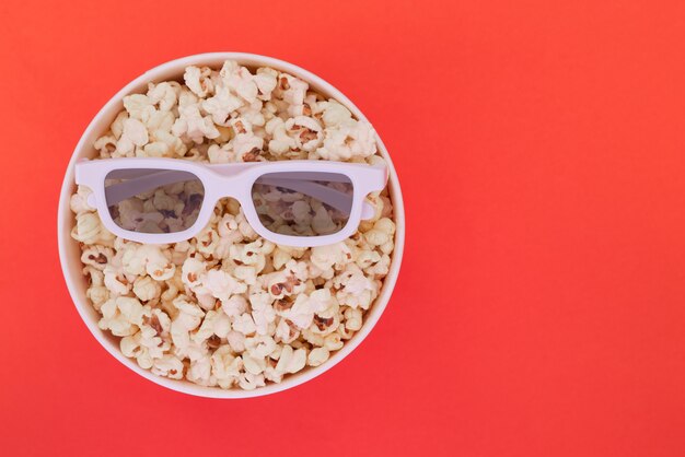 Lunettes 3D se trouvent sur une tasse de pop-corn isolé sur fond rouge. Concept de cinéma.