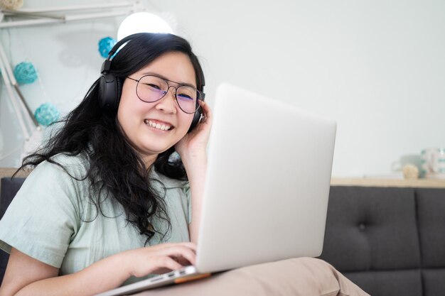 Lunettes belle femme asiatique travaille sur son ordinateur portable dans la chambre avec un thème de couleur marron vert pastel