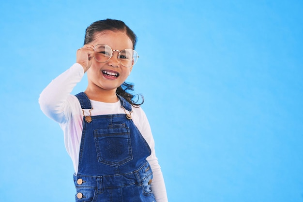 Lunettes et cadre pour petite fille en portrait en studio pour la santé visuelle et les soins oculaires sur fond bleu Lunettes de test pour enfants féminins et jeune mannequin avec lentille sourire ou vue avec espace de maquette