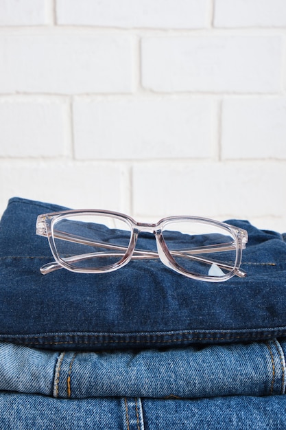 Lunettes élégantes sur une pile de jeans sur l'espace de copie de fond de mur de briques