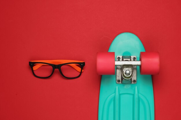 Lunettes élégantes sans lentilles, planche de croisière sur fond rouge. Équipement de hipster. Vue de dessus