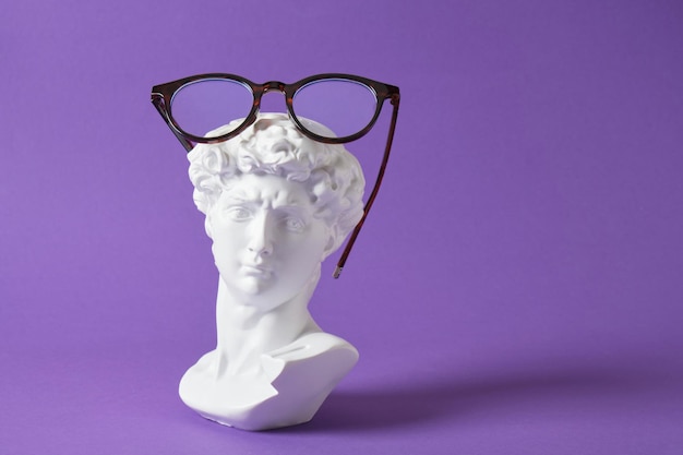 Photo lunettes élégantes avec sculpture en gypse sur fond de couleur violet tendance, copiez l'espace buste de david