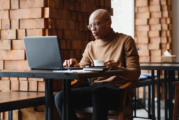 Des lunettes d'étudiants noirs sérieux prenant des notes assis à table avec un ordinateur portable et travaillant sur un projet dans un café confortable.