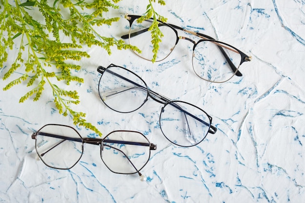 Lunettes de femme et branches de petites fleurs jaunes sur fond texturé Mise à plat