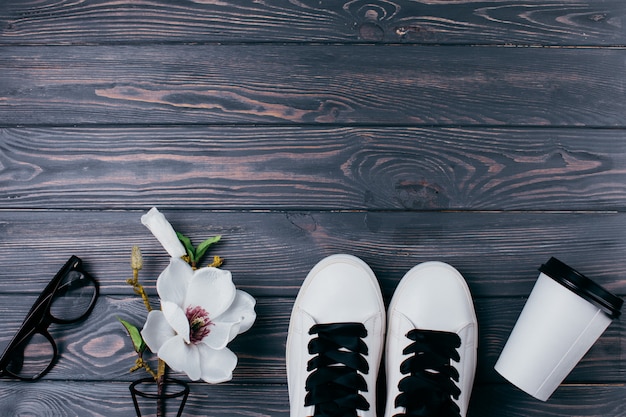 Lunettes, fleur d&#39;orchidée, baskets blanches et gobelet en papier sur un bois