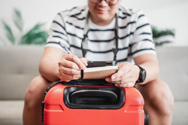 Des lunettes d'homme asiatique préparent des vêtements dans des valises Il choisit des documents de voyage de vêtements l'itinéraire pour un voyage en solo et vérifie la liste de contrôle Voyage vacances et concept de vacances