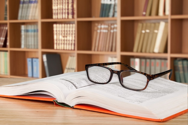 Lunettes de lecture noires en gros plan et livre sur fond flou de bibliothèque