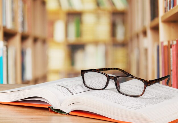 Lunettes de lecture noires en gros plan et livre sur fond flou de bibliothèque