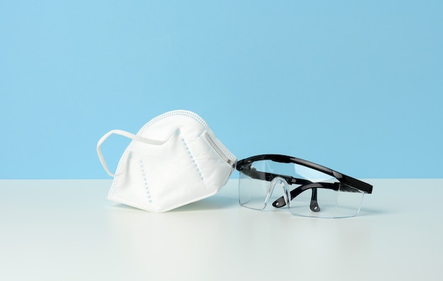 Lunettes médicales de protection en plastique transparent et masque jetable blanc sur fond bleu