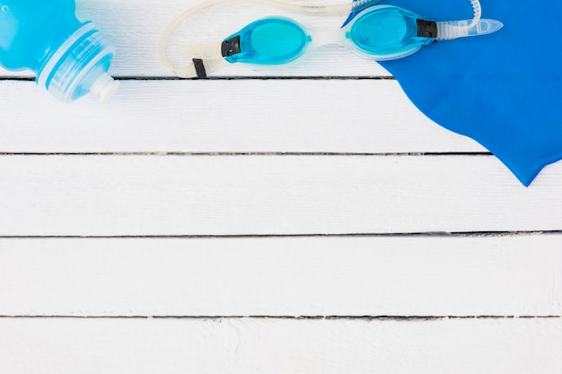 Photo lunettes de natation bleues; bouteille d'eau et serviette de table sur une table en bois blanche