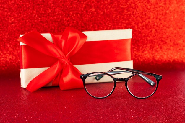 Photo lunettes noires sur fond de paillettes rouges festives avec une boîte cadeau