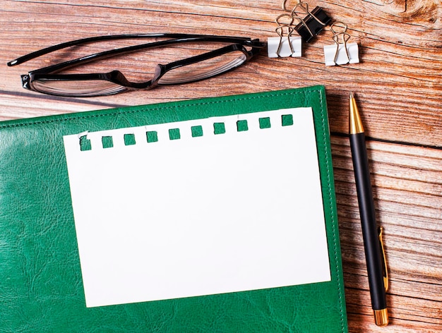 Photo lunettes noires trombones noir et blanc un stylo un bloc-notes vert et une feuille de papier avec un espace pour insérer du texte sur un bureau en bois vue de dessus d'un lieu de travail élégant espace de copie