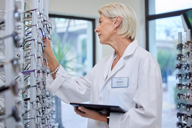 Lunettes d'optométriste et professionnel dans un magasin de détail ou un opticien regardant les spécifications ou les lentilles de prescription Vision et femme mûre choisissant des montures de lunettes et des lunettes dans un magasin d'optique