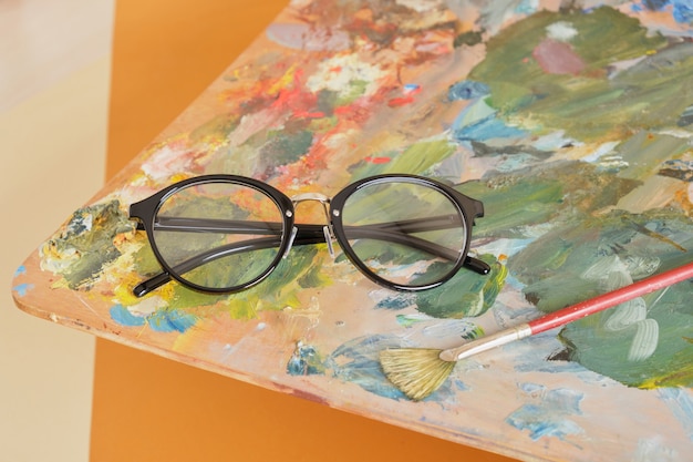 Lunettes sur une palette avec des peintures sur fond marron, concept d'atelier d'artiste