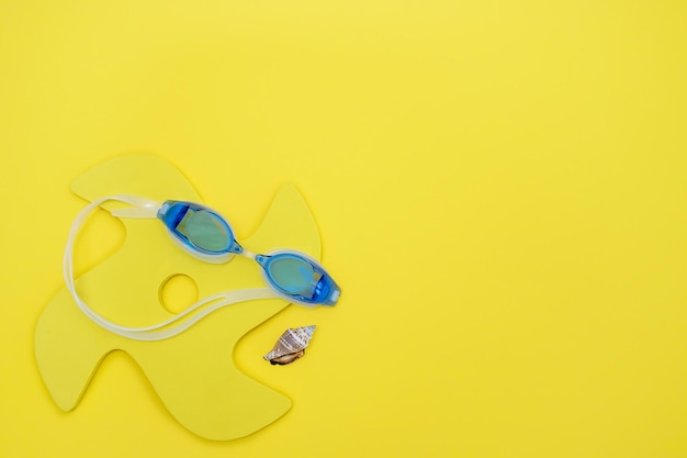 Lunettes pour nager un jouet et une coquille sur fond jaune avec espace de copie