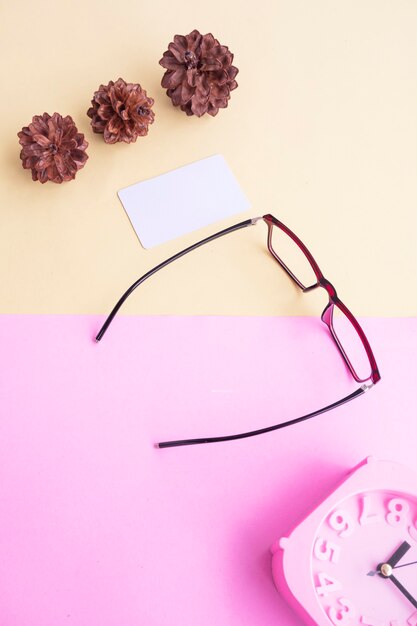 Lunettes, réveil, fleurs de pin sur fond rose pastel et jaune pastel. Concept d'été, concept minimal