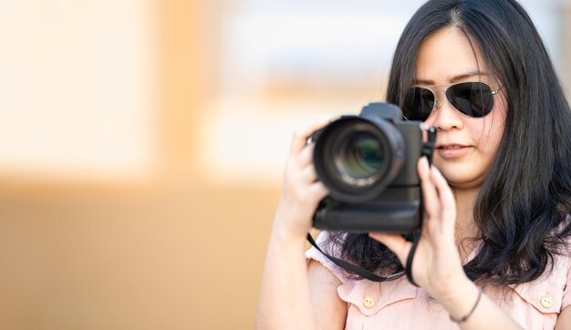 Lunettes de soleil amateur Asian Woman prendre une photo avec un appareil photo sans miroir professionnel à l'extérieur du bâtiment sur le toit bleu au crépuscule