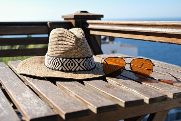 Lunettes de soleil chapeau de paille sur terrasse en bois vue mer et piscine