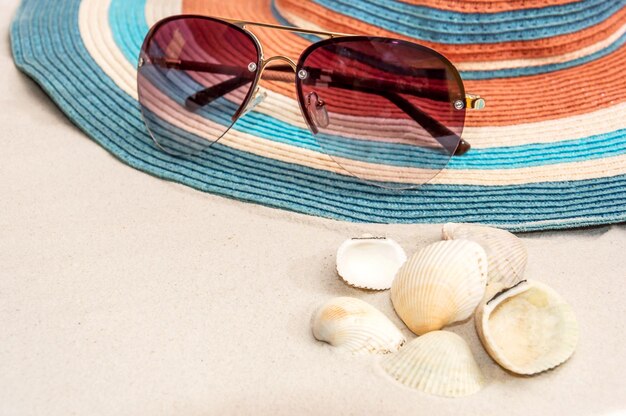 Lunettes de soleil chapeau de plage et coquillages sur le sable