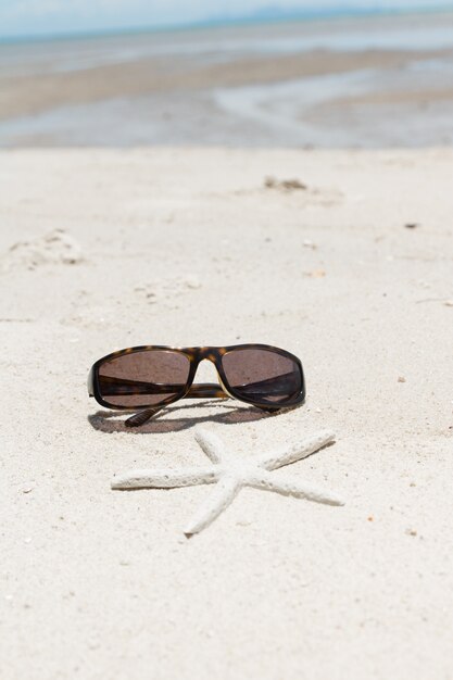 Lunettes de soleil chic et étoile de mer sur la plage de sable blanc