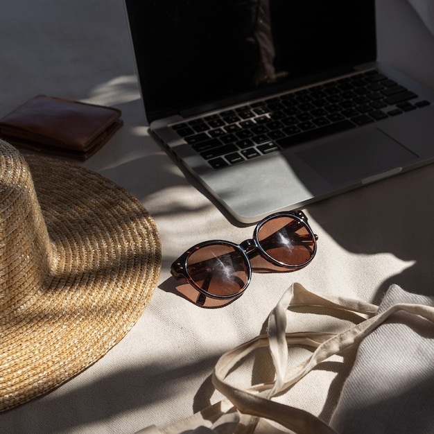 Lunettes de soleil féminines élégantes, chapeau de paille, sac shopping, ordinateur portable sur un canapé blanc avec oreillers.