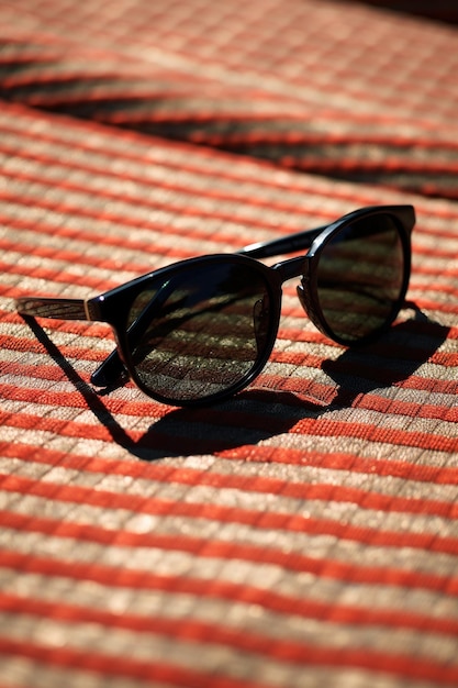 Photo lunettes de soleil noires brillantes posées sur un tapis tissé noir en plein soleil