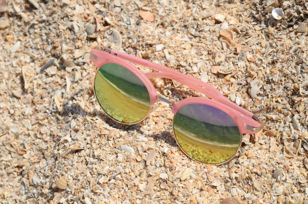 Lunettes de soleil roses contre le soleil sur le sable de la plage