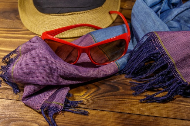 Lunettes de soleil rouges, chapeau de paille et écharpe d'été sur fond en bois. Accessoires de mode pour femmes. Vacances d'été et concept de voyage