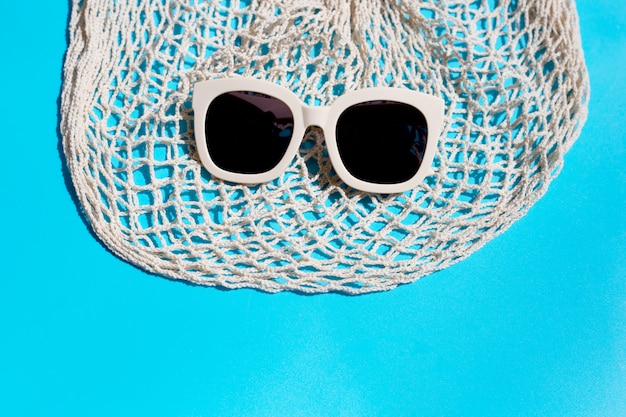 Lunettes de soleil avec sac en filet sur fond bleu. Profitez du concept de vacances.