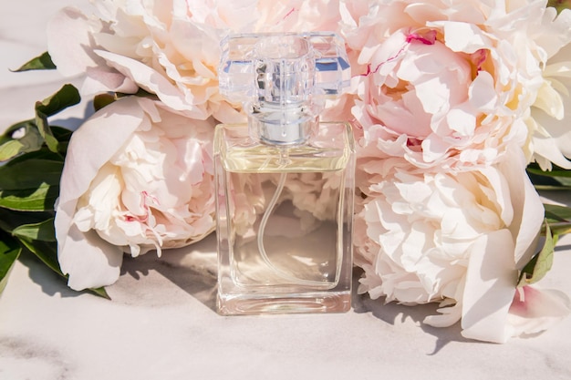 Une luxueuse bouteille de parfum féminin ou d'eau de toilette sur fond de délicates pivoines vue de face présentation d'un produit cosmétique