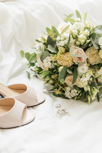 Un luxueux bouquet de mariée avec des roses blanches à côté de chaussures et d'accessoires sur fond clair