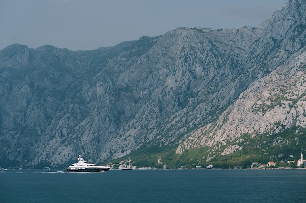 Luxueux yacht à moteur blanc navigue le long de la baie de Kotor avec des montagnes