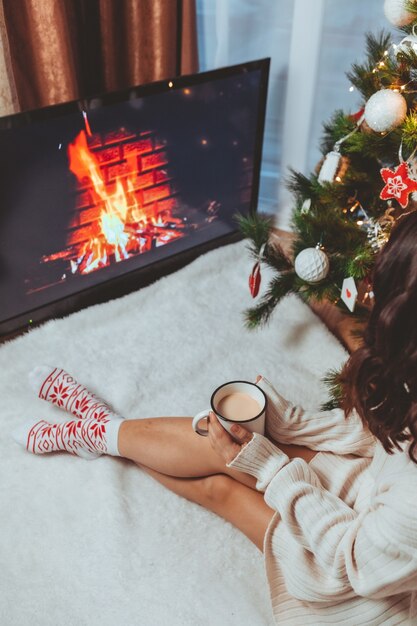 Lviv, Ukraine - 15 décembre 2021 : jeune jolie femme assise près d'un arbre de Noël buvant une tasse de café copie espace