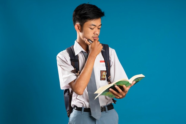 Lycéen indonésien pensant en regardant le livre qu'il porte sur fond bleu