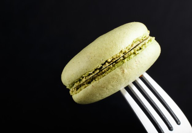 Macaron vert unique ou gâteau de macaron sur une fourchette sur le mur noir. vue de côté, gros plan.