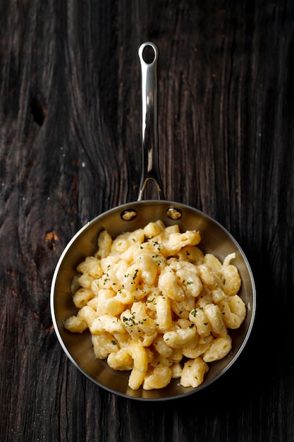 Macaroni crémeux et fromage sur une poêle Oan avec parmesan et herbes, isolé sur table en bois, vue de dessus