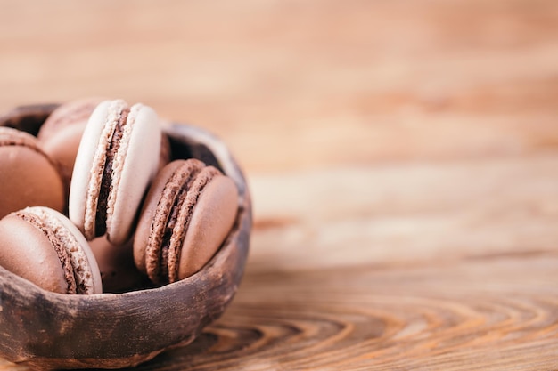 Des macarons au chocolat et à la vanille faits maison dans un bol en céramique sur un fond en bois