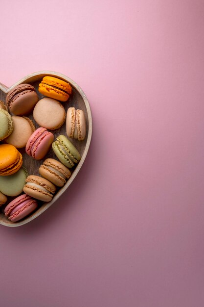 Macarons biscuits colorés dans un bol de coeur en bois Macarons dessert sucré français vue de dessus fond rose Copy space