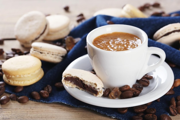 Macarons colorés doux et café dans une tasse sur fond de table en bois