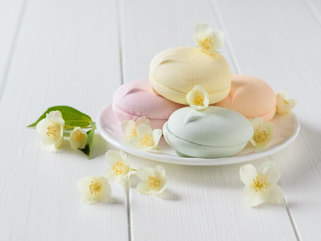 Macarons colorés avec des fleurs de jasmin sur une table en bois blanc