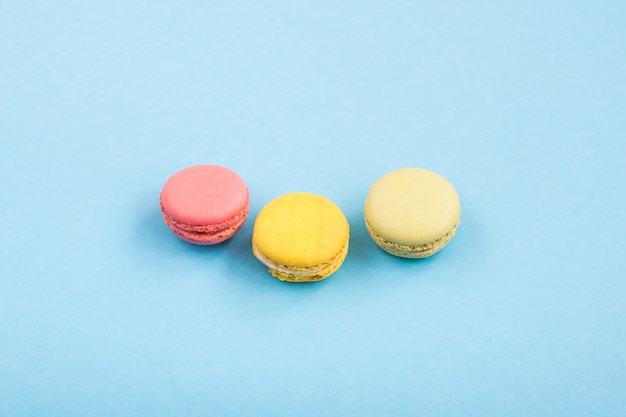 Macarons colorés, macarons roses, jaunes et verts sur fond bleu. Bonbons, desserts. Copyplace, place pour le texte.