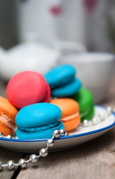 Macarons colorés en plaque blanche sur table en bois.