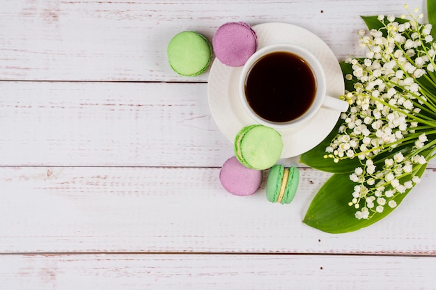 Macarons colorés une tasse de café et de muguet sur fond de bois libre mise à plat