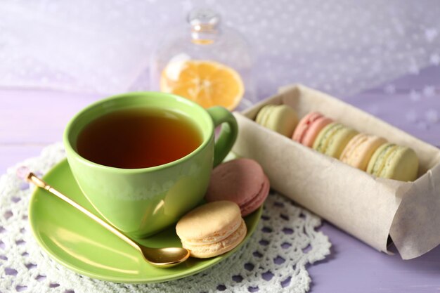 Macarons colorés avec une tasse de thé sur fond de bois