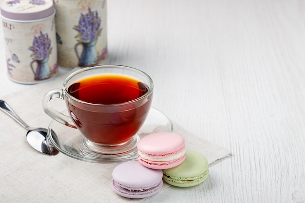 Macarons colorés et une tasse de thé sur une table de cuisine en bois clair