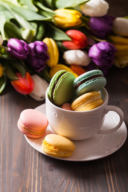 Macarons de couleur dans une tasse et fleurs en arrière-plan