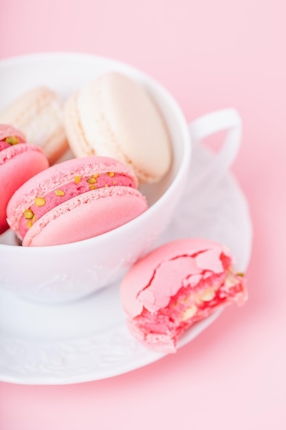 Macarons de couleur rose et crème dans une tasse en porcelaine blanche sur fond rose