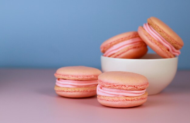 macarons à la crème au beurre de framboise sur une grille de cuisson, fond bleu avec espace de copie