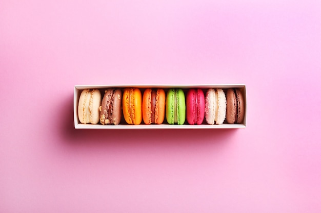 Macarons français colorés dans une boîte cadeau sur fond rose